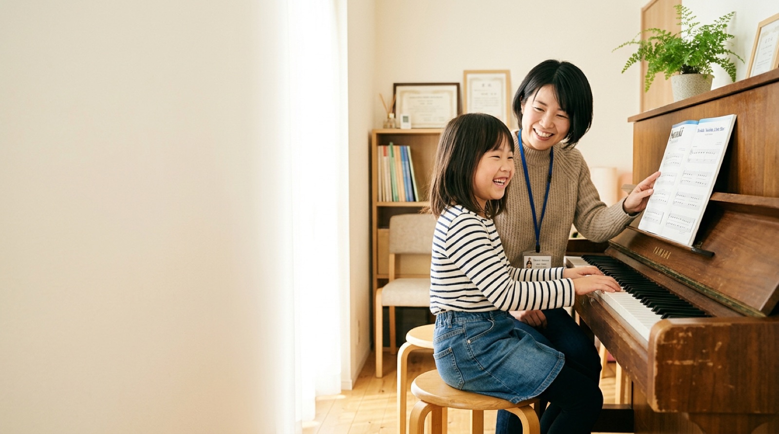 アップライトピアノを弾く女の子に楽譜を示して笑う講師